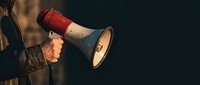 Person holding red and white megaphone for announcements and communication in dramatic lighting with copy space for marketing campaigns.