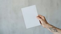 Hand holding blank white paper sheet against gray concrete wall background for mockup and branding purposes.