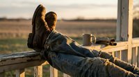 Farmer resting with boots up on rustic fence at golden sunset, coffee mug nearby, open field in background, rural countryside lifestyle.