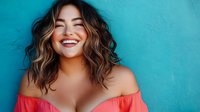 Young Asian woman with wavy brown hair laughing genuinely against turquoise wall, wearing coral off-shoulder top. Natural beauty and authentic joy expression for lifestyle content.