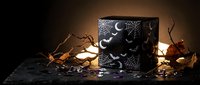 Mystical black candle with moon phases and celestial symbols glowing warmly among autumn leaves creating magical atmospheric lighting for spiritual rituals.