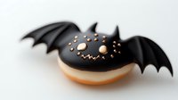 Black bat-shaped donut with wings and orange sprinkles on white background, Halloween-themed pastry dessert for seasonal celebration and party treats.