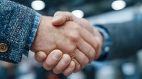 Business handshake between two professionals in suits sealing deal or partnership agreement in modern office environment with blurred background lights.