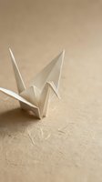 White origami paper crane on beige textured surface with soft natural lighting creating peaceful zen atmosphere for meditation and mindfulness concepts.