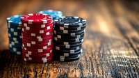 Stacks of red, blue and black poker chips on rustic wooden table with dramatic lighting and shallow depth of field, creating atmospheric gambling scene.