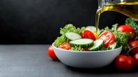 Fresh garden salad with lettuce, cherry tomatoes, cucumber slices in white bowl while pouring olive oil, dark background with copy space. Food photography.