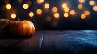 Orange pumpkin on dark wooden table against blurred golden bokeh lights background, creating magical autumn atmosphere for seasonal decoration.