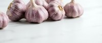 Fresh purple garlic bulbs with papery skin arranged on white marble surface, suitable for cooking, food photography, culinary blogs, and recipe illustrations.