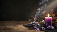 Purple candle burning with mystical smoke, crystal ball, amethyst gems and dried lavender on rustic wooden table creating magical witchcraft atmosphere.