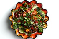 Fresh mixed salad with arugula, cherry tomatoes, red onions and colorful bell peppers served in vibrant orange ceramic bowl on white background.