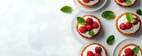 Fresh raspberry tartlets with sweet cream filling and mint leaves on white background, top view with copy space for menu or recipe design.