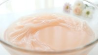 Cosmetic cream or gel with peachy tone swirled in glass bowl, isolated on white background for skincare product design and packaging mockups.