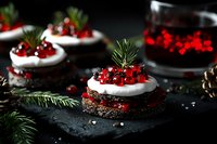 Festive chocolate mini cakes topped with white cream, fresh red currants and pine sprigs on dark stone background. Holiday dessert with dramatic lighting.