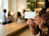 Woman holding blank white card in modern office lobby with colleagues in background, suitable for business marketing and corporate communications.