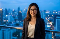Professional Asian businesswoman in glasses and blazer standing on urban balcony at twilight with city skyline background for corporate presentations.