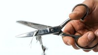 Young adult male with medium brown skin tone holding open black scissors with metal blades against white background, suitable for tool, office supply, and craft-related design projects.