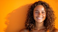 Young Hispanic woman with curly brown hair and bright genuine smile against vibrant orange background, radiating happiness and confidence in casual lifestyle portrait.