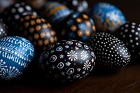 Decorated Easter eggs in blue and black with intricate folk art patterns featuring dots, swirls and floral designs on dark wooden surface, selective focus.