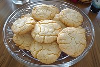 Homemade crinkle sugar cookies with distinctive cracked surface texture arranged on clear glass plate, fresh baked golden treats for holiday dessert.