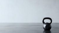 Black kettlebell on wooden floor against white wall in minimalist gym setting for fitness and strength training workouts.