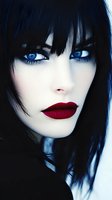 Close-up portrait of Asian woman with striking blue eyes, dark hair, and bold red lipstick against dark background, creating dramatic contrast and mysterious atmosphere.