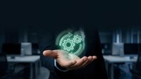 Businessman holding glowing gear mechanism hologram in open palm representing innovation and technology solutions in modern office environment.