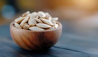 Salted pumpkin seeds in wooden bowl on dark rustic table with blurred background, healthy snack and nutritious food concept for natural eating.