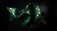 Elegant emerald green silk ribbon with gold foil accents flowing gracefully against dark background for luxury fashion and premium packaging design.