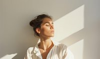 Young Hispanic woman in white shirt with eyes closed enjoying sunlight through window, peaceful meditation moment with dramatic shadow pattern on wall.