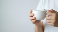 Close-up of hands holding a white ceramic mug against neutral background, suitable for beverage, lifestyle, and branding mockup projects.