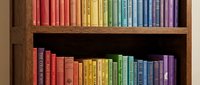 Colorful rainbow books arranged on wooden shelves creating organized library display for education and reading concepts in home or office interior.