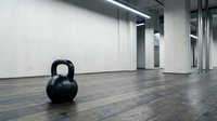 Kettlebell weight on wooden floor in modern gym studio with concrete walls and natural light from windows.