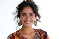 Beautiful young Hispanic woman with curly dark hair and bright smile wearing colorful ethnic pattern dress and ornate earrings against white background, perfect for lifestyle and beauty content.