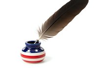 Isolated brown feather resting in patriotic red, white and blue striped inkwell with stars, symbolizing American writing, journalism and creative expression for design projects.