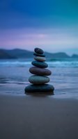 Balanced stone cairn on serene beach at twilight with purple and blue sky creating peaceful meditation and wellness atmosphere for mindfulness practices.