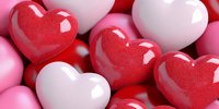 Glossy red, pink and white heart shapes in close-up view create romantic composition with soft shadows and reflective surfaces. Suitable for Valentine's Day designs.