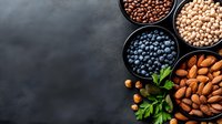 Fresh organic nuts, legumes and berries in black bowls on dark concrete background with copy space. Healthy protein-rich ingredients for vegan diet.