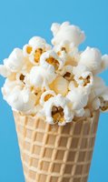 Fresh popped white popcorn overflowing from golden waffle ice cream cone against bright blue background for creative food photography and snack concepts.