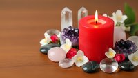 Red candle burning surrounded by healing crystals, gemstones and white flowers on wooden surface for meditation, spa treatments and wellness rituals.