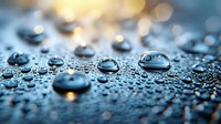 Water drops on dark hydrophobic surface with golden bokeh lights creating dramatic macro photography effect. Natural condensation pattern shows surface tension.