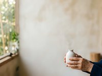 Hands holding white ceramic vase against neutral wall background. Suitable for home decor, pottery, crafts, interior design, and lifestyle content.