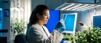 Female scientist examining plant samples in modern laboratory with grow lights for agricultural research and biotechnology development.