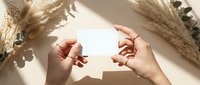 Female hands holding blank white card mockup with dried pampas grass and eucalyptus branches creating natural shadows on neutral beige background.