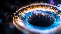 Glowing optical fiber ring with blue and gold light streaks creating futuristic technology pattern against dark background. Macro photography.