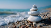 Balanced stack of smooth stones on beach with gentle waves and pebbles in background, soft focus creates peaceful zen atmosphere for wellness and meditation.