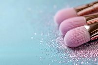 Pink makeup brushes with scattered glitter on mint background, soft focus close-up view. Professional cosmetic tools for beauty and glamour applications.