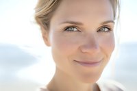 Young blonde Caucasian woman with natural makeup smiling softly in bright sunlight. Close-up portrait with warm lighting for wellness and lifestyle content.