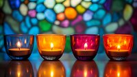Colorful glass candle holders with glowing flames against vibrant stained glass background creating atmospheric mood lighting for spiritual or festive occasions.