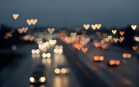 Romantic heart-shaped bokeh lights creating dreamy atmosphere over blurred city street at dusk. Valentine's Day background with warm golden illumination.