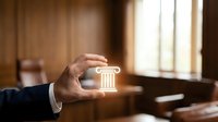 Professional businessman hand holding glowing pillar icon in elegant office interior representing legal services, law firm consultation and justice concepts.